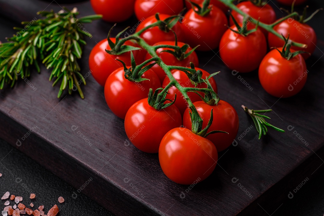 Deliciosos tomates cereja frescos em um galho com especiarias e ervas sobre um fundo escuro de concreto
