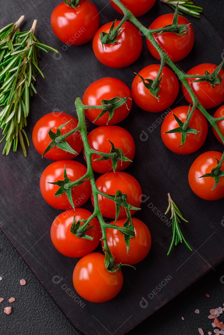 Deliciosos tomates cereja frescos em um galho com especiarias e ervas sobre um fundo escuro de concreto