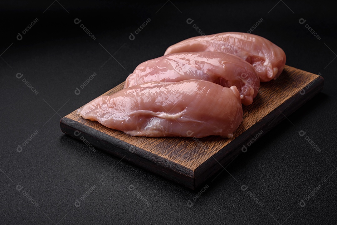 Pedaços de frango cru ou filé de peru com sal, especiarias e ervas sobre um fundo escuro de concreto