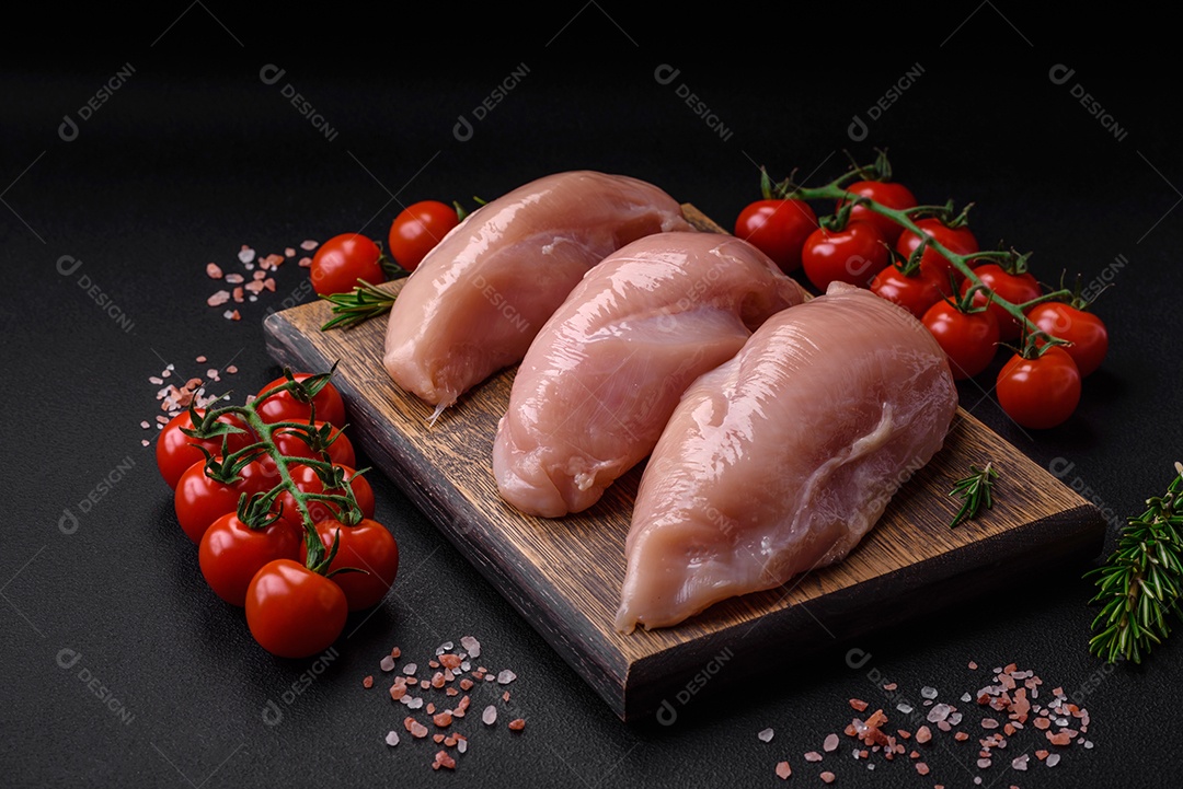 Pedaços de frango cru ou filé de peru com sal, especiarias e ervas sobre um fundo escuro de concreto