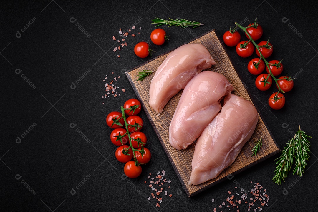 Pedaços de frango cru ou filé de peru com sal, especiarias e ervas sobre um fundo escuro de concreto