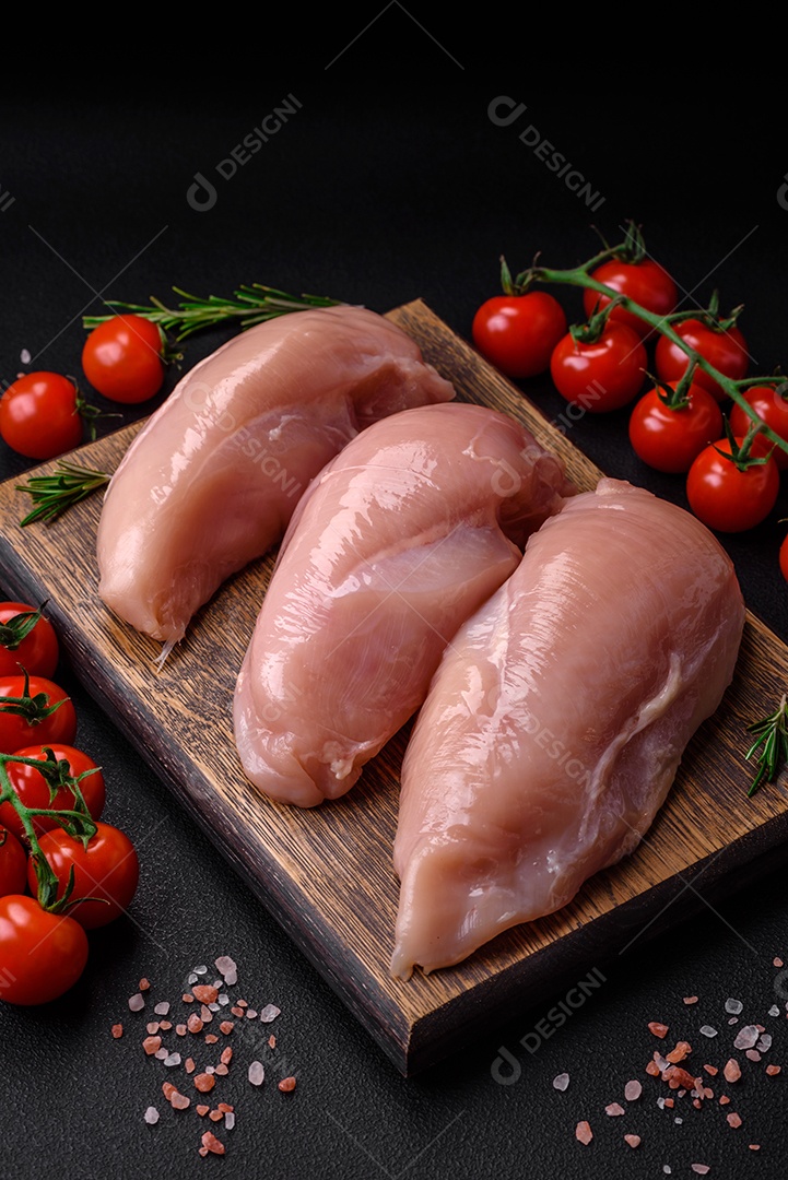 Pedaços de frango cru ou filé de peru com sal, especiarias e ervas sobre um fundo escuro de concreto