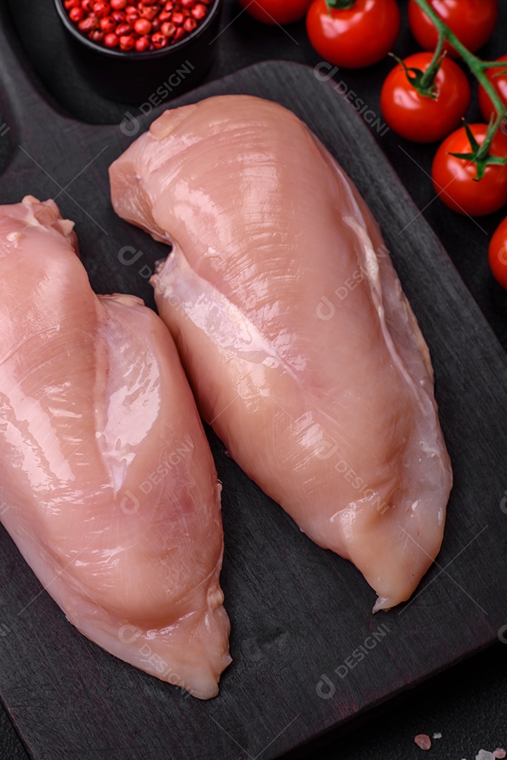 Pedaços de frango cru ou filé de peru com sal, especiarias e ervas sobre um fundo escuro de concreto