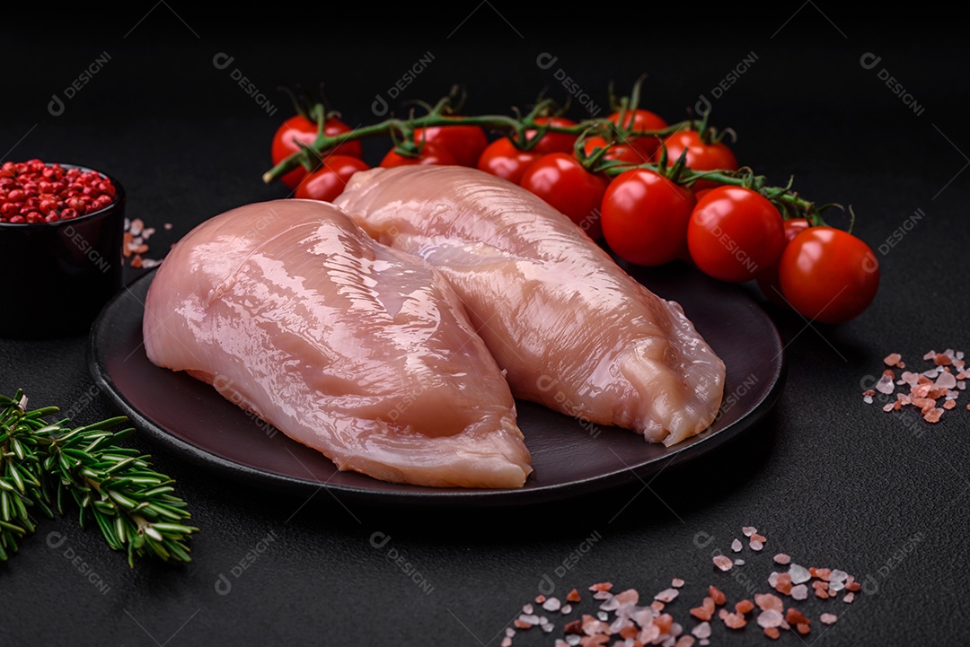 Pedaços de frango cru ou filé de peru com sal, especiarias e ervas sobre um fundo escuro de concreto