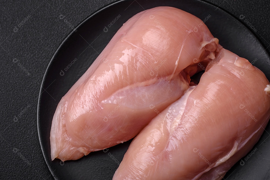 Pedaços de frango cru ou filé de peru com sal, especiarias e ervas sobre um fundo escuro de concreto