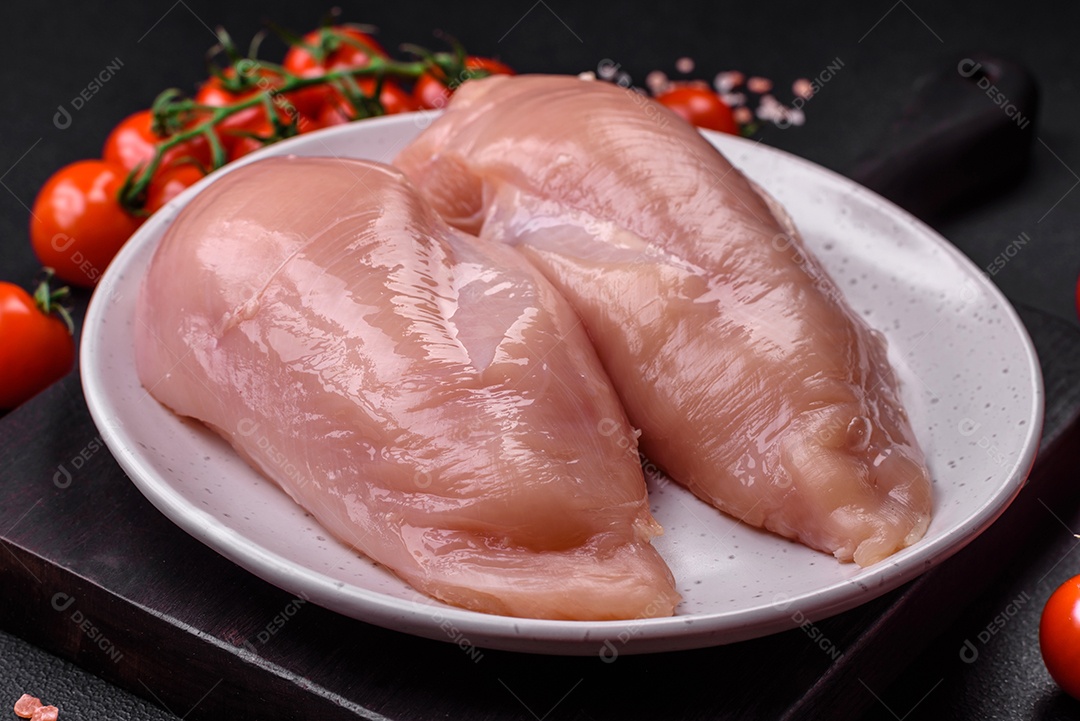 Pedaços de frango cru ou filé de peru com sal, especiarias e ervas sobre um fundo escuro de concreto