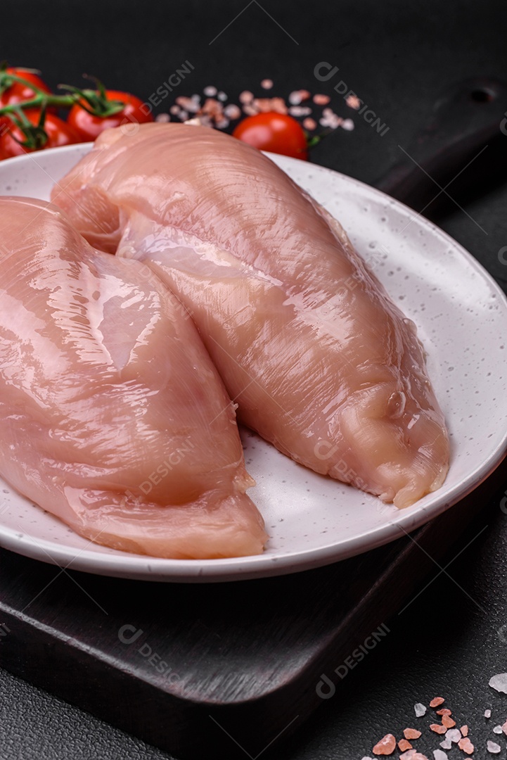 Pedaços de frango cru ou filé de peru com sal, especiarias e ervas sobre um fundo escuro de concreto