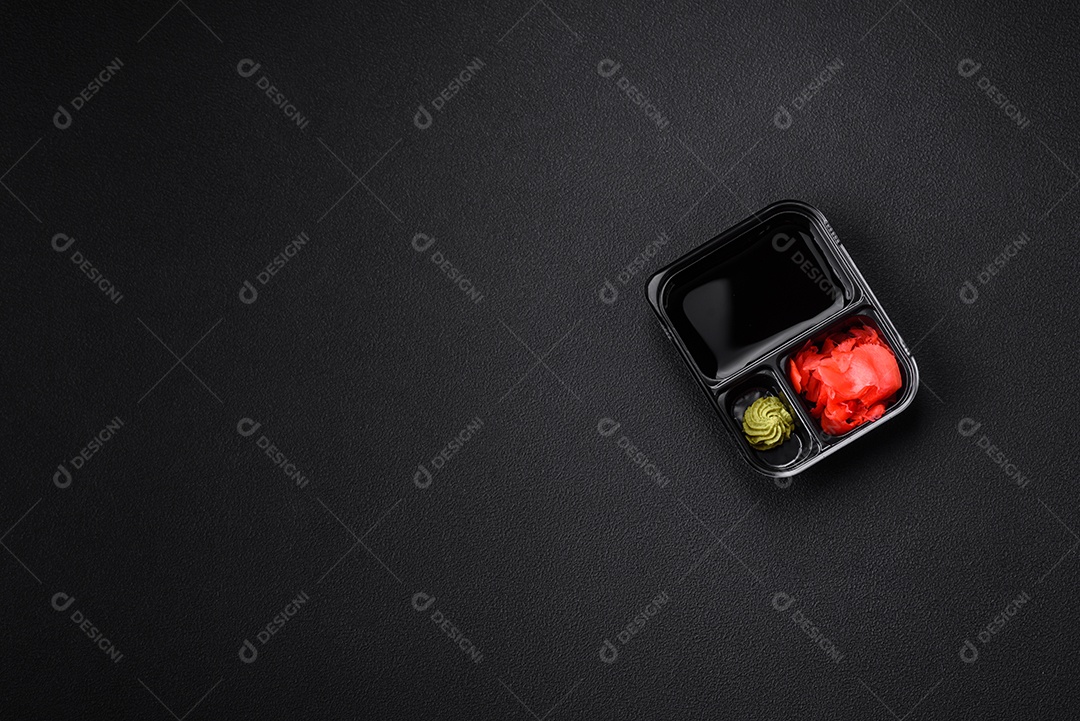 Gengibre em conserva, molho de soja e wasabi em recipientes de plástico porcionados sobre um fundo escuro de concreto