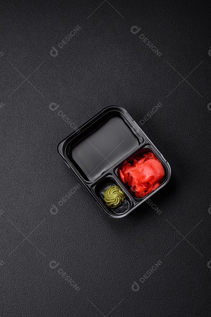 Gengibre em conserva, molho de soja e wasabi em recipientes de plástico porcionados sobre um fundo escuro de concreto