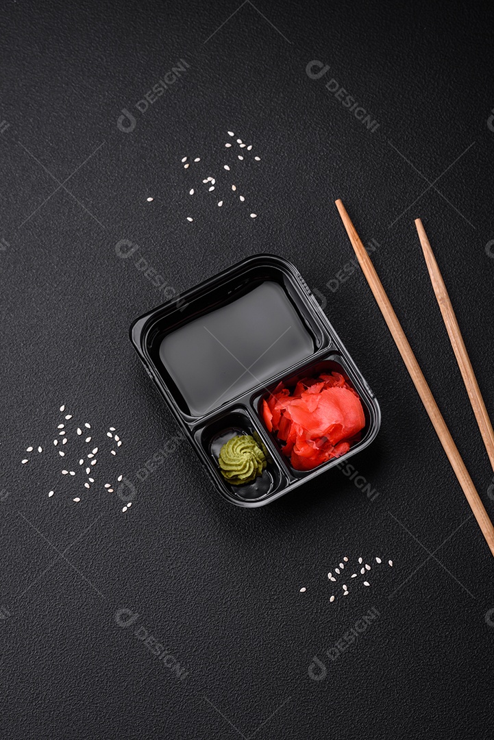 Gengibre em conserva, molho de soja e wasabi em recipientes de plástico porcionados sobre um fundo escuro de concreto