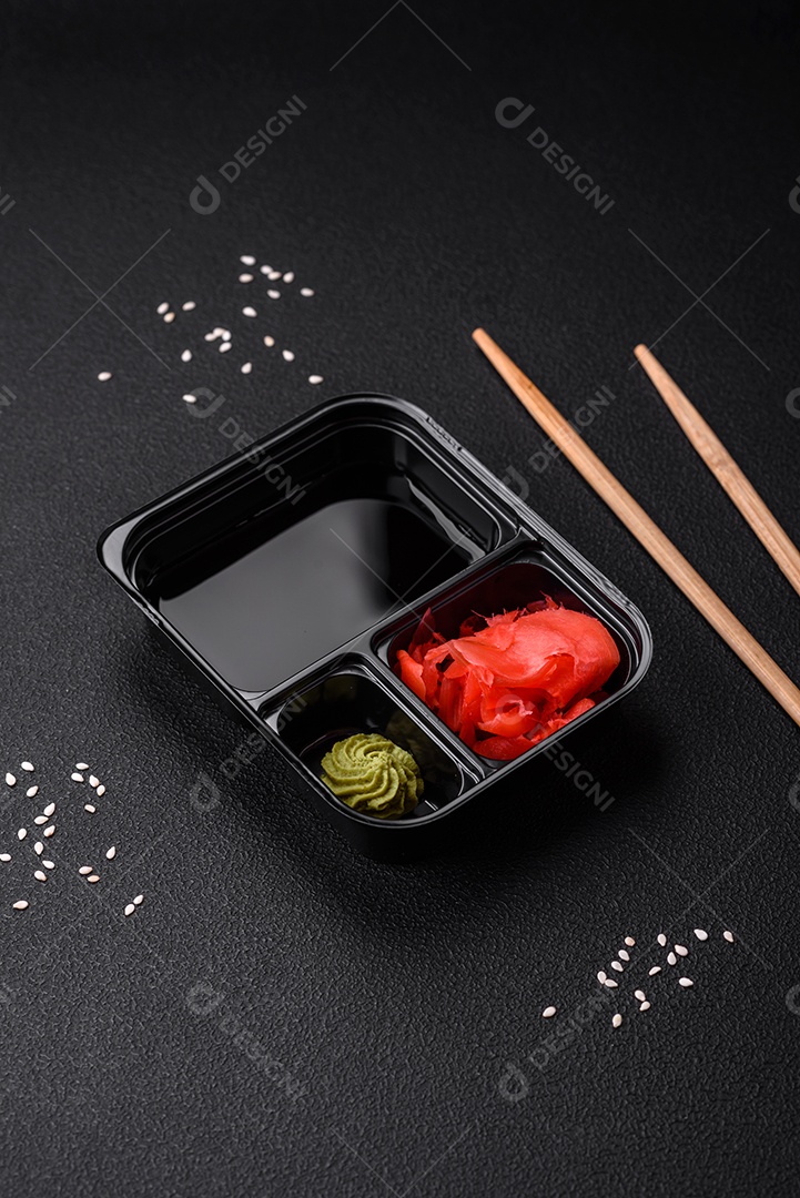 Gengibre em conserva, molho de soja e wasabi em recipientes de plástico porcionados sobre um fundo escuro de concreto