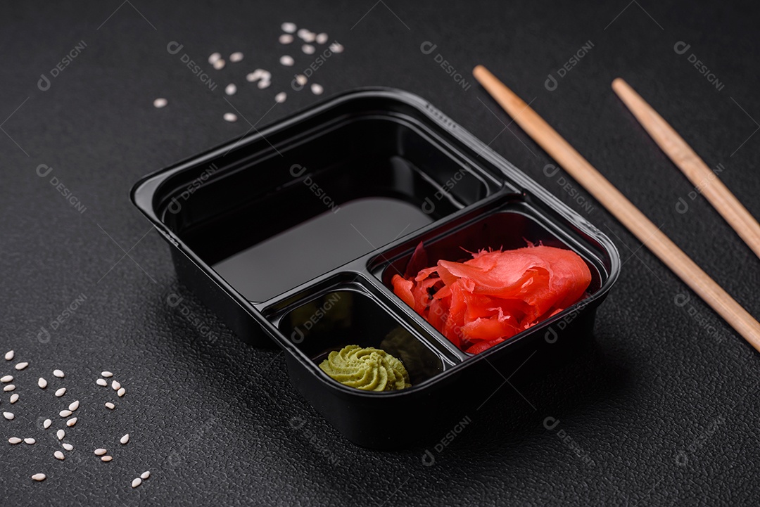 Gengibre em conserva, molho de soja e wasabi em recipientes de plástico porcionados sobre um fundo escuro de concreto