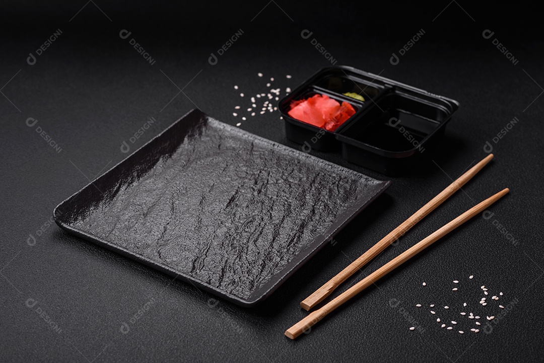 Gengibre em conserva, molho de soja e wasabi em recipientes de plástico porcionados sobre um fundo escuro de concreto