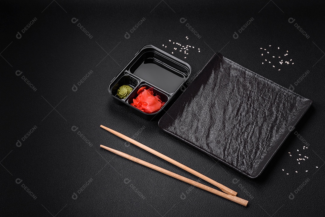 Gengibre em conserva, molho de soja e wasabi em recipientes de plástico porcionados sobre um fundo escuro de concreto