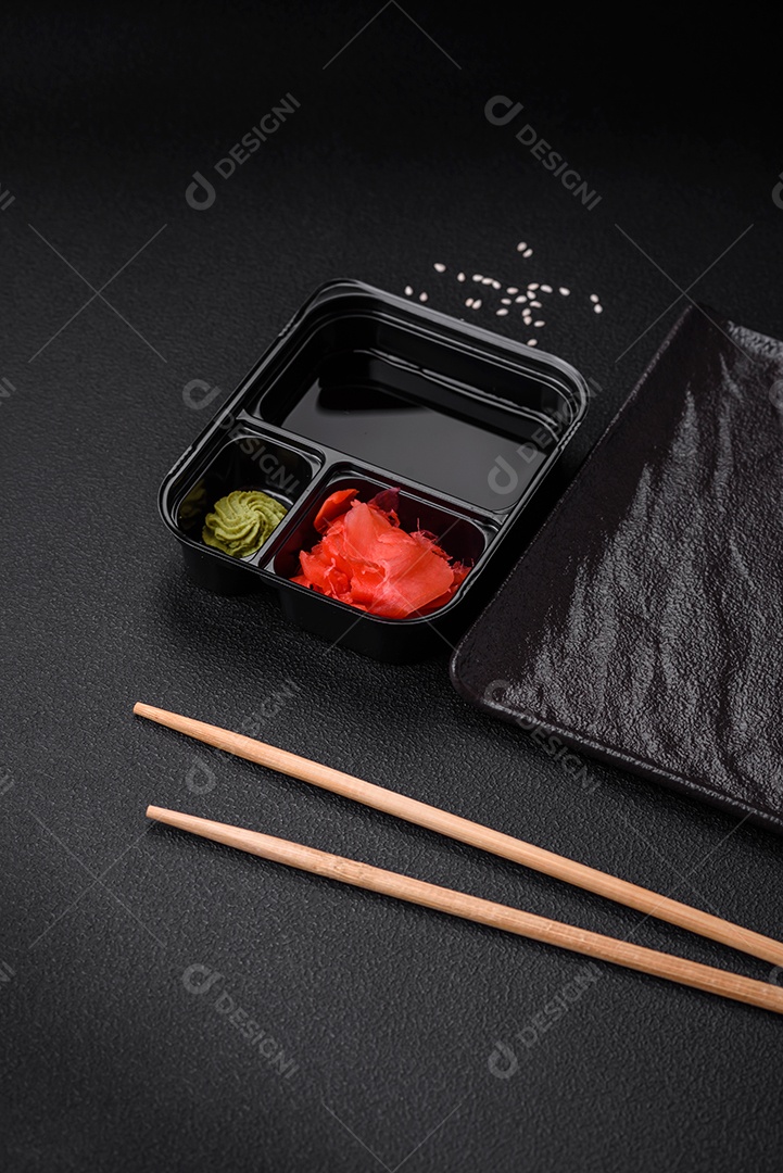 Gengibre em conserva, molho de soja e wasabi em recipientes de plástico porcionados sobre um fundo escuro de concreto