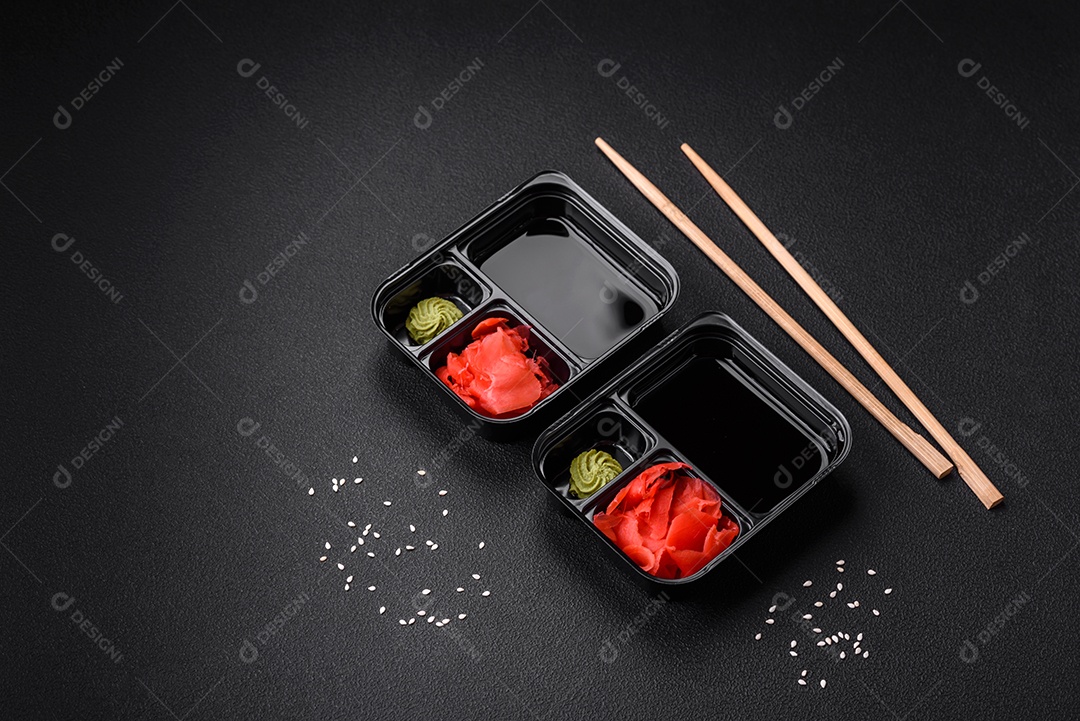 Gengibre em conserva, molho de soja e wasabi em recipientes de plástico porcionados sobre um fundo escuro de concreto