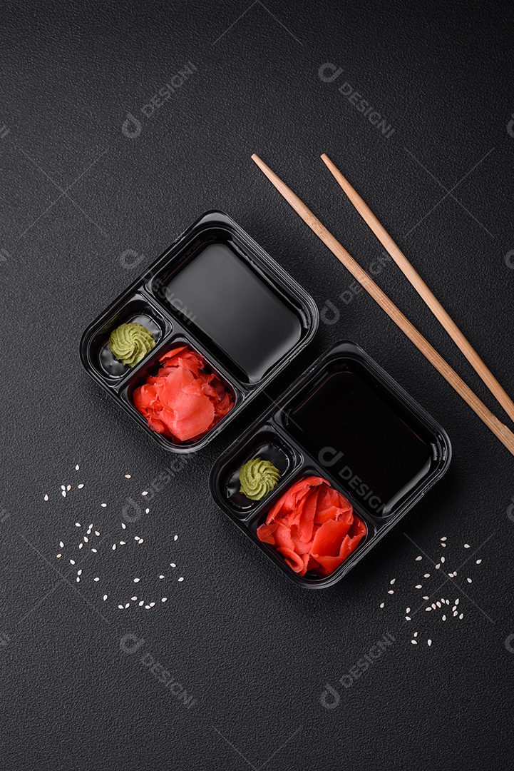 Gengibre em conserva, molho de soja e wasabi em recipientes de plástico porcionados sobre um fundo escuro de concreto