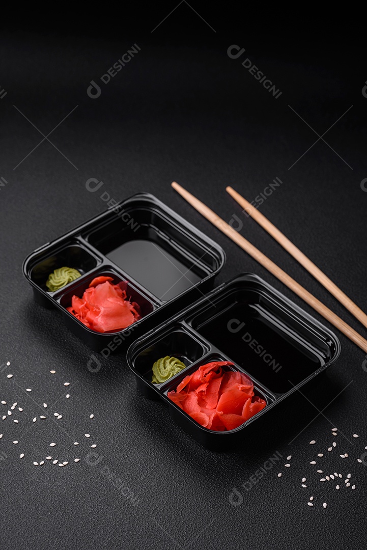Gengibre em conserva, molho de soja e wasabi em recipientes de plástico porcionados sobre um fundo escuro de concreto