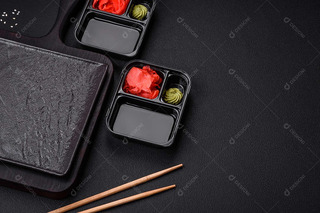 Gengibre em conserva, molho de soja e wasabi em recipientes de plástico porcionados sobre um fundo escuro de concreto