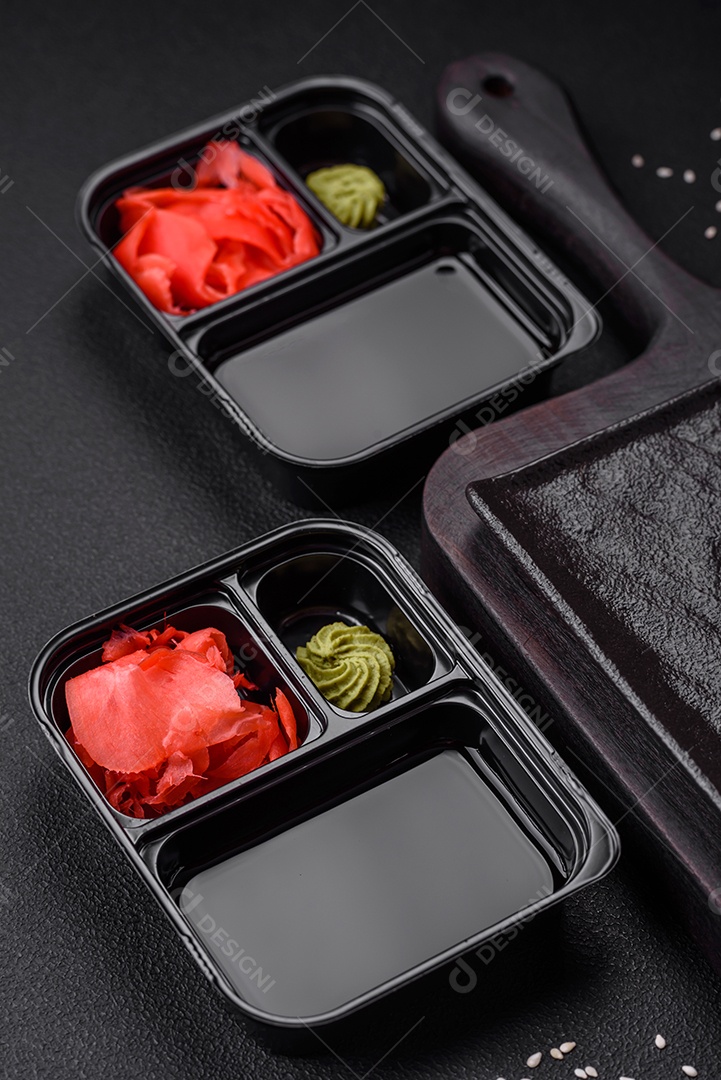 Gengibre em conserva, molho de soja e wasabi em recipientes de plástico porcionados sobre um fundo escuro de concreto