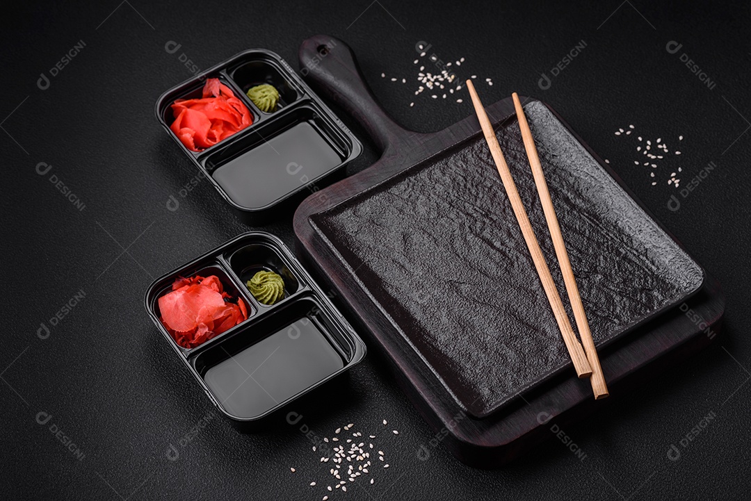 Gengibre em conserva, molho de soja e wasabi em recipientes de plástico porcionados sobre um fundo escuro de concreto