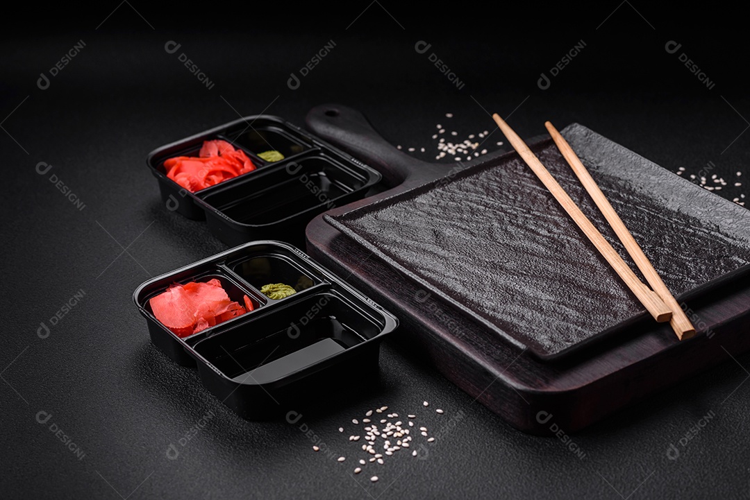 Gengibre em conserva, molho de soja e wasabi em recipientes de plástico porcionados sobre um fundo escuro de concreto