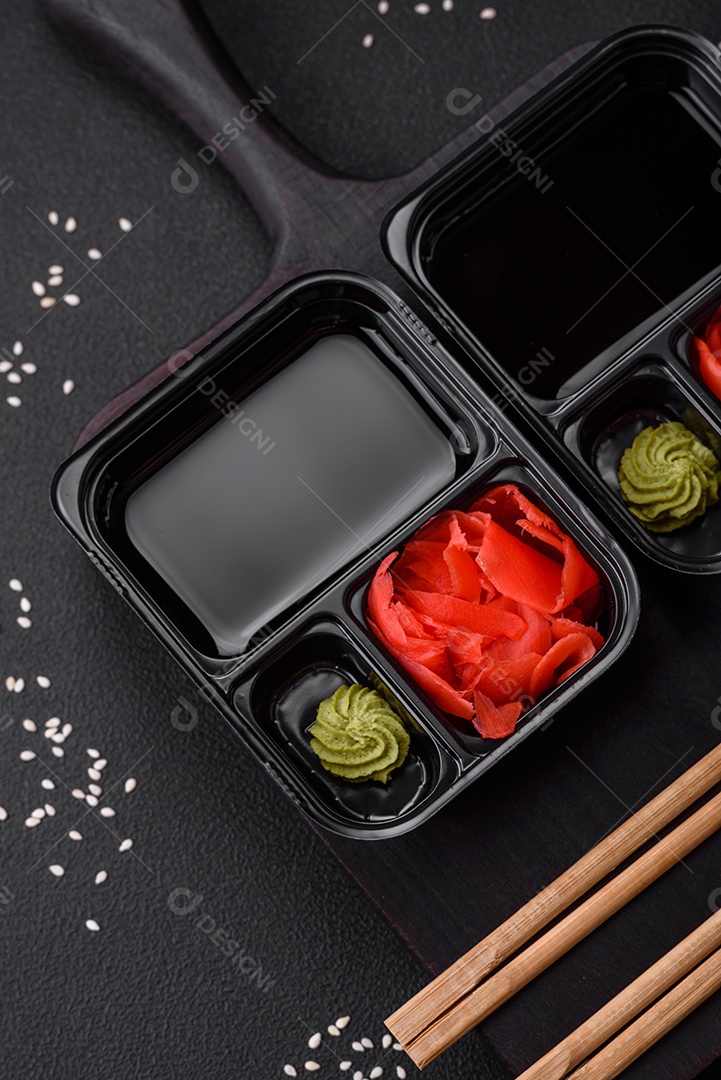 Gengibre em conserva, molho de soja e wasabi em recipientes de plástico porcionados sobre um fundo escuro de concreto