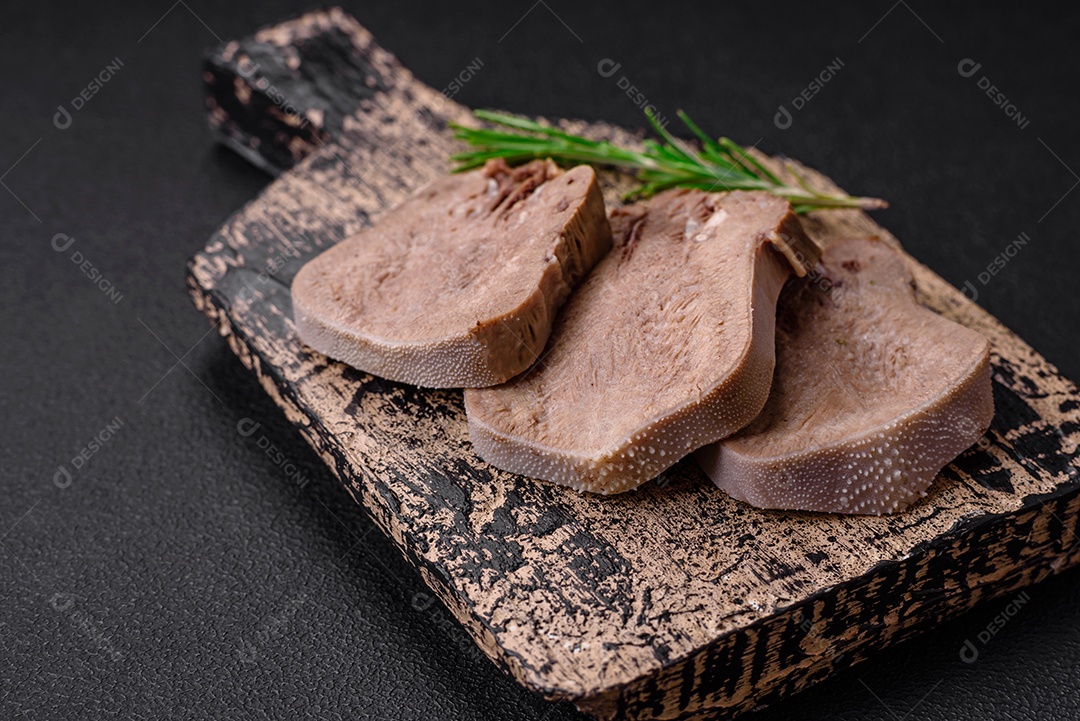 Deliciosa língua de boi cozida cortada com legumes e especiarias em um fundo escuro de concreto