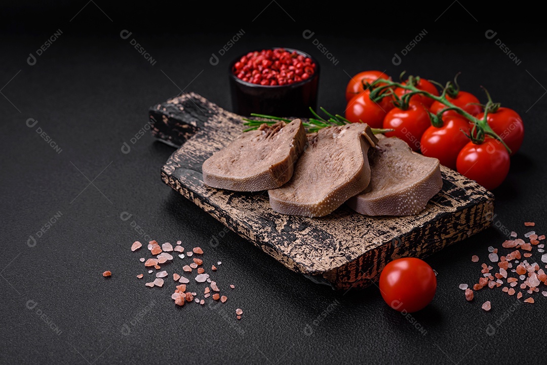 Deliciosa língua de boi cozida cortada com legumes e especiarias em um fundo escuro de concreto