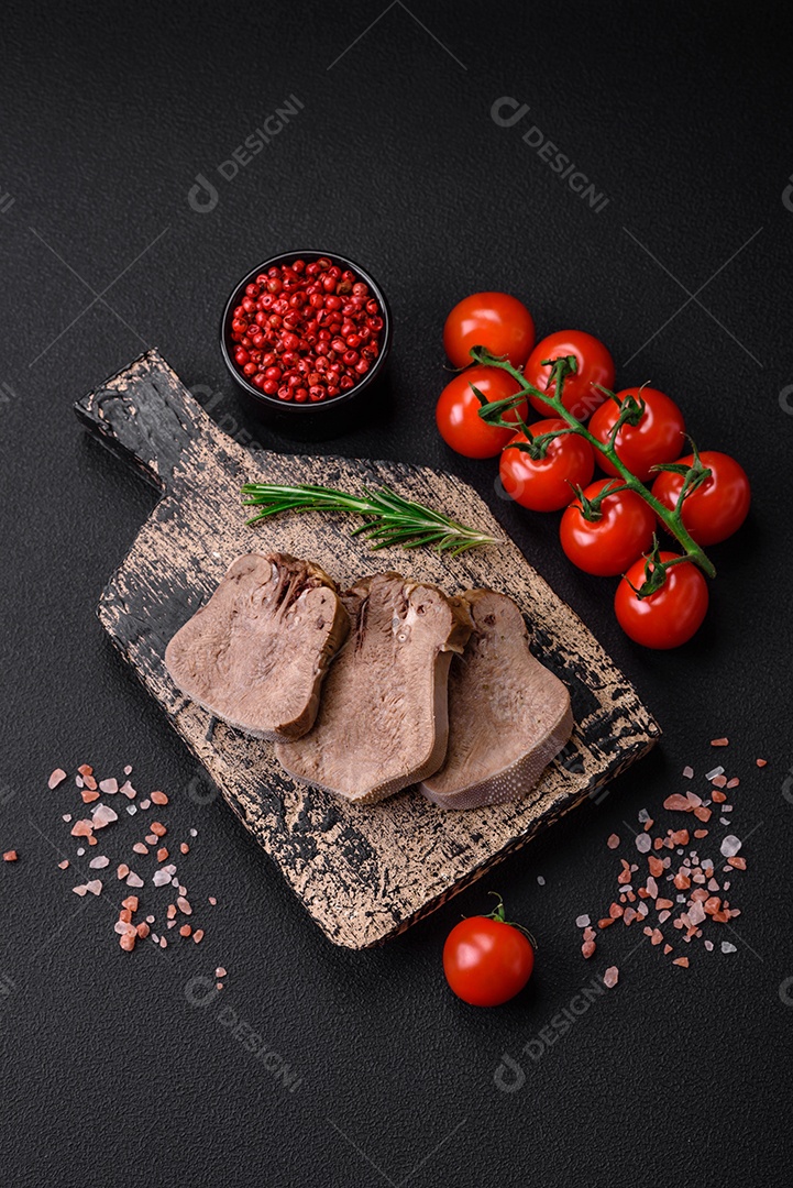 Deliciosa língua de boi cozida cortada com legumes e especiarias em um fundo escuro de concreto