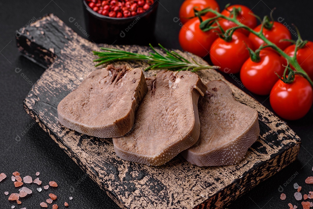 Deliciosa língua de boi cozida cortada com legumes e especiarias em um fundo escuro de concreto