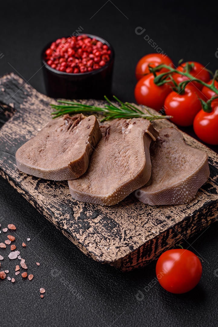 Deliciosa língua de boi cozida cortada com legumes e especiarias em um fundo escuro de concreto