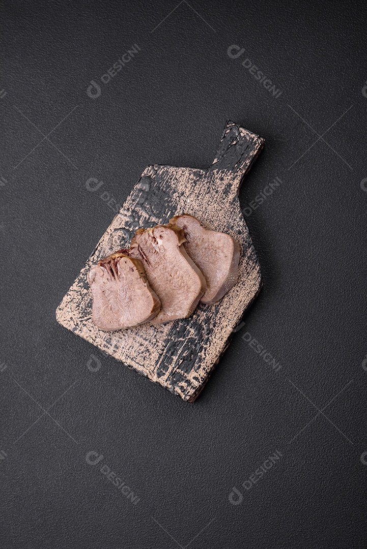 Deliciosa língua de boi cozida cortada com legumes e especiarias em um fundo escuro de concreto