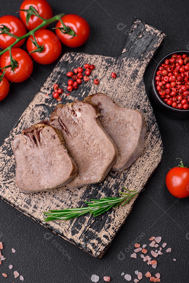 Deliciosa língua de boi cozida cortada com legumes e especiarias em um fundo escuro de concreto