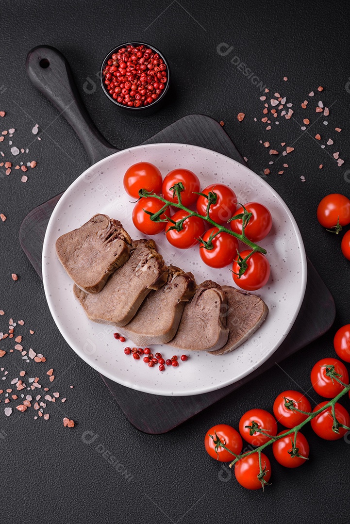 Deliciosa língua de boi cozida cortada com legumes e especiarias em um fundo escuro de concreto