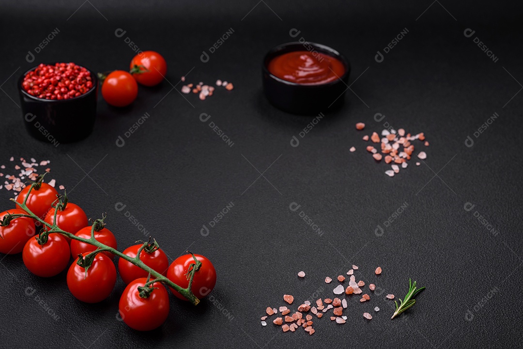 Deliciosos tomates cereja frescos em um galho com especiarias e ervas sobre um fundo escuro de concreto