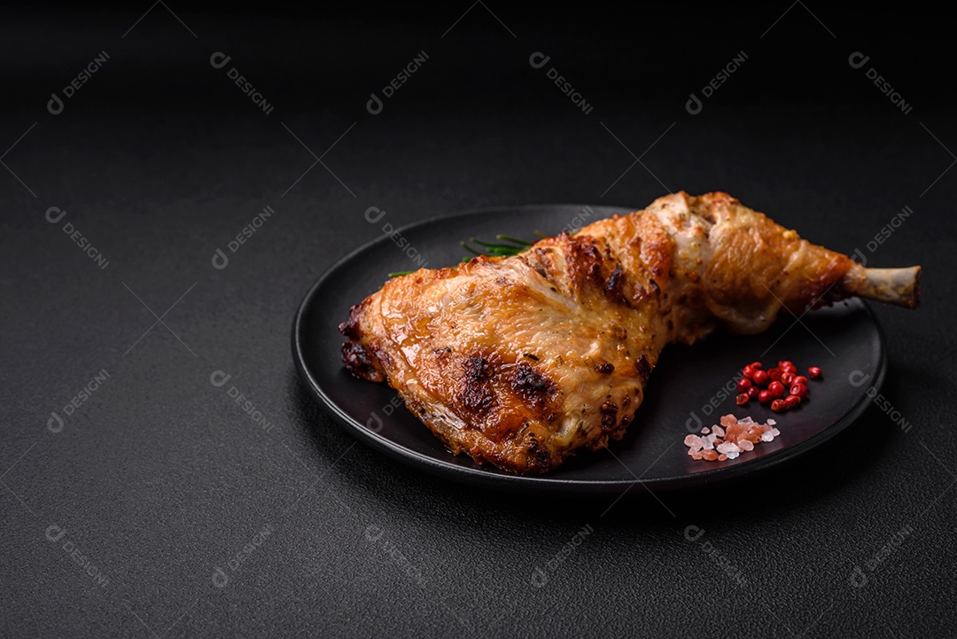 Perna de frango grelhado fresco com sal, especiarias e ervas sobre um fundo escuro de concreto