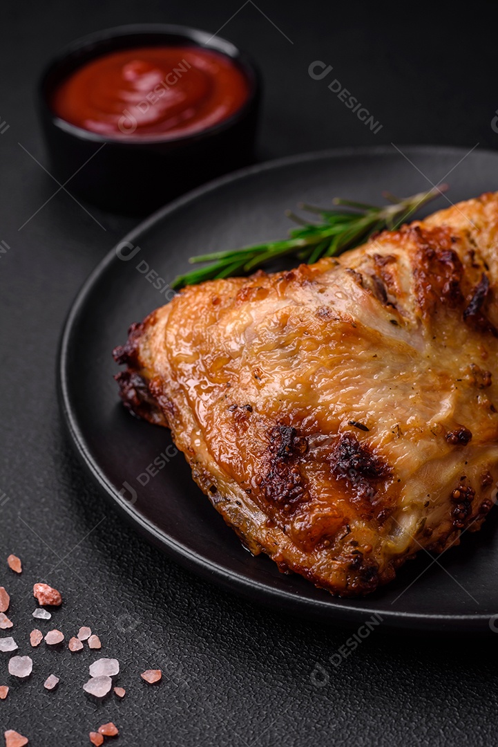 Perna de frango grelhado fresco com sal, especiarias e ervas sobre um fundo escuro de concreto