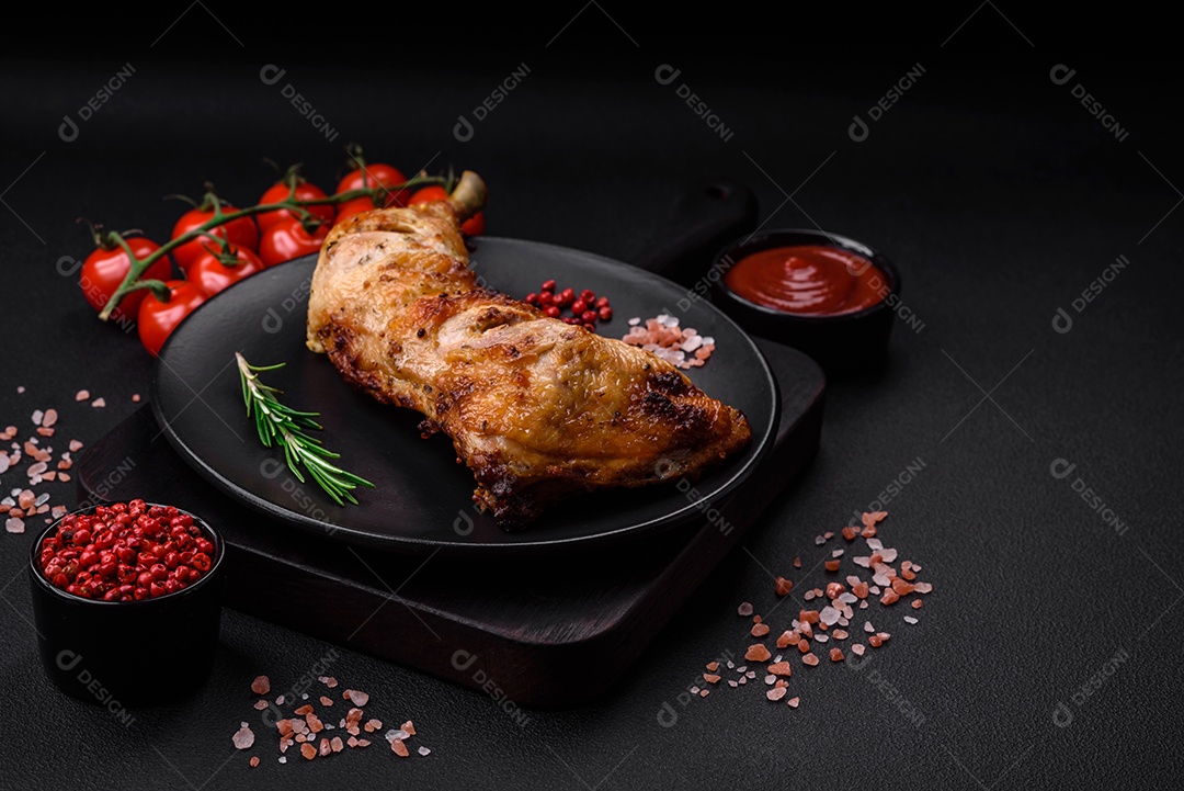 Perna de frango grelhado fresco com sal, especiarias e ervas sobre um fundo escuro de concreto