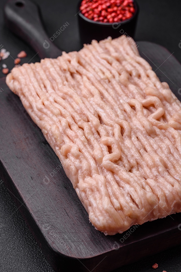 Frango picado fresco com sal, especiarias e ervas em uma tábua de madeira sobre um fundo escuro de concreto