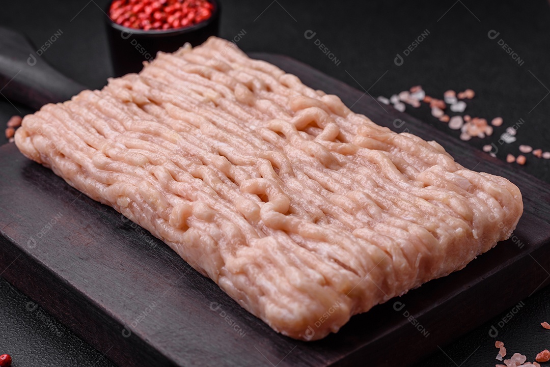 Frango picado fresco com sal, especiarias e ervas em uma tábua de madeira sobre um fundo escuro de concreto