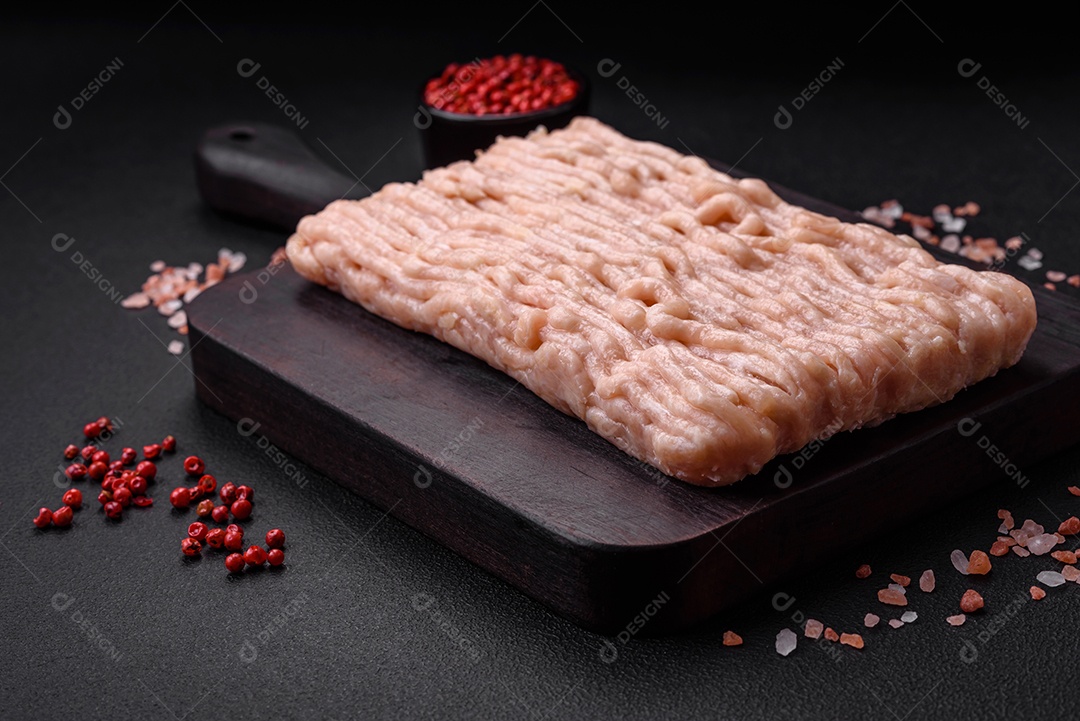 Frango picado fresco com sal, especiarias e ervas em uma tábua de madeira sobre um fundo escuro de concreto
