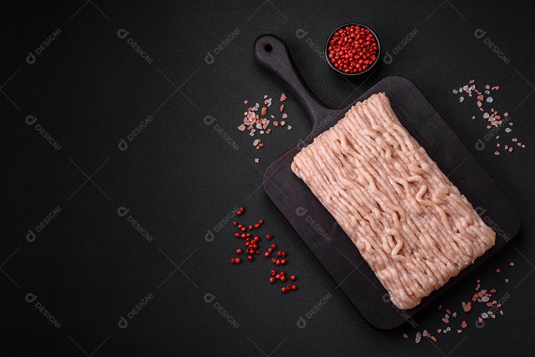 Frango picado fresco com sal, especiarias e ervas em uma tábua de madeira sobre um fundo escuro de concreto