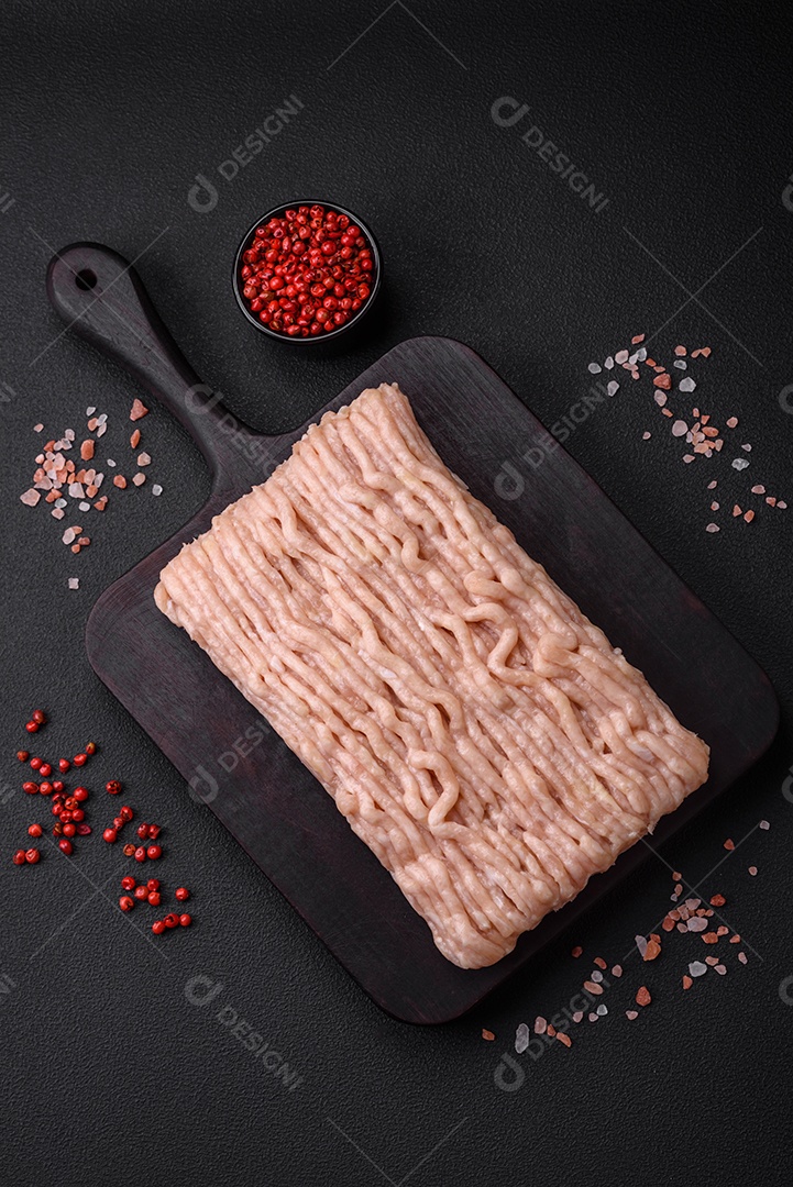 Frango picado fresco com sal, especiarias e ervas em uma tábua de madeira sobre um fundo escuro de concreto