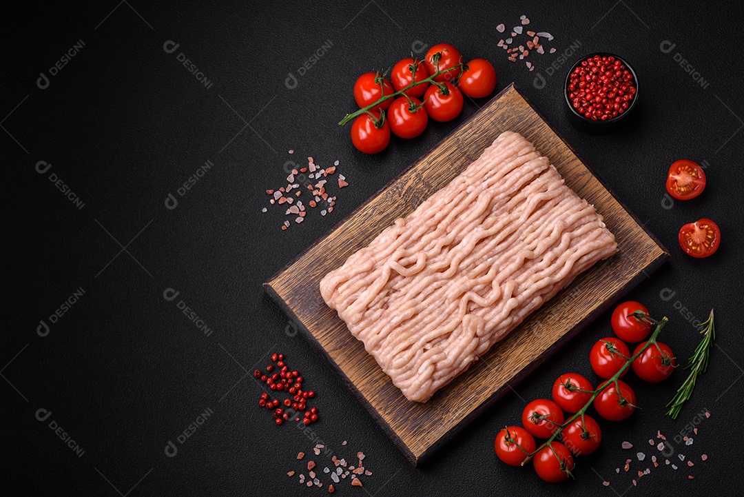 Frango picado fresco com sal, especiarias e ervas em uma tábua de madeira sobre um fundo escuro de concreto
