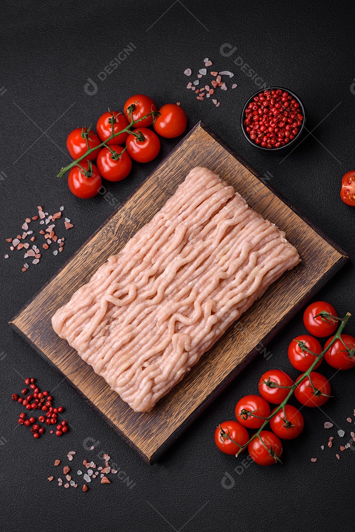 Frango picado fresco com sal, especiarias e ervas em uma tábua de madeira sobre um fundo escuro de concreto