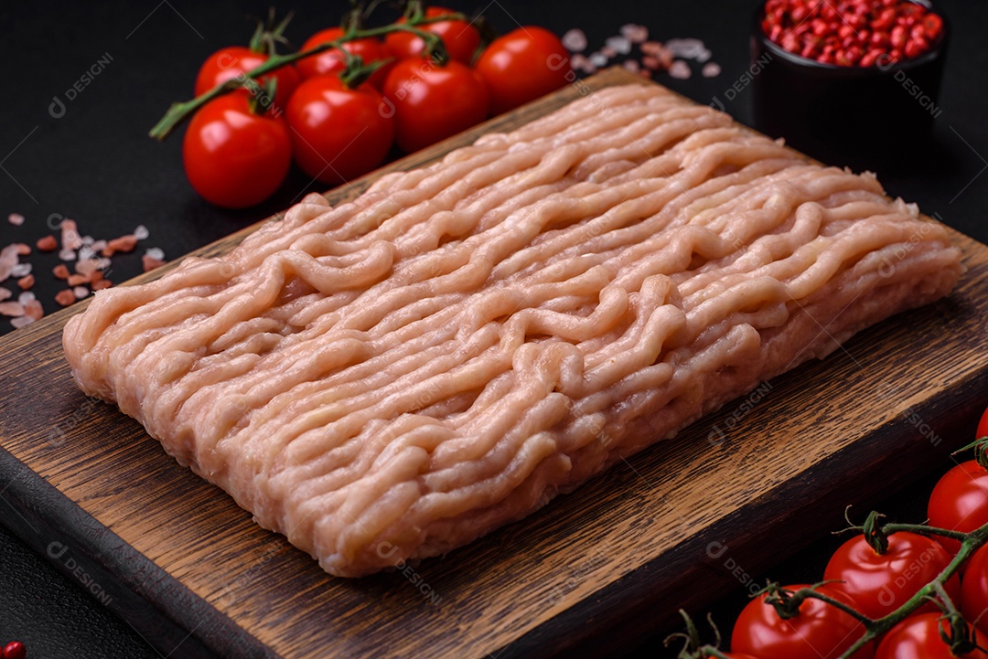 Frango picado fresco com sal, especiarias e ervas em uma tábua de madeira sobre um fundo escuro de concreto