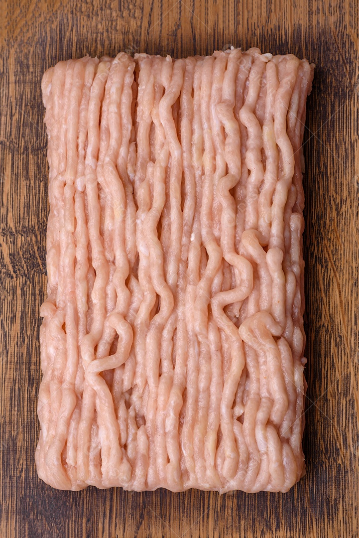 Frango picado fresco com sal, especiarias e ervas em uma tábua de madeira sobre um fundo escuro de concreto