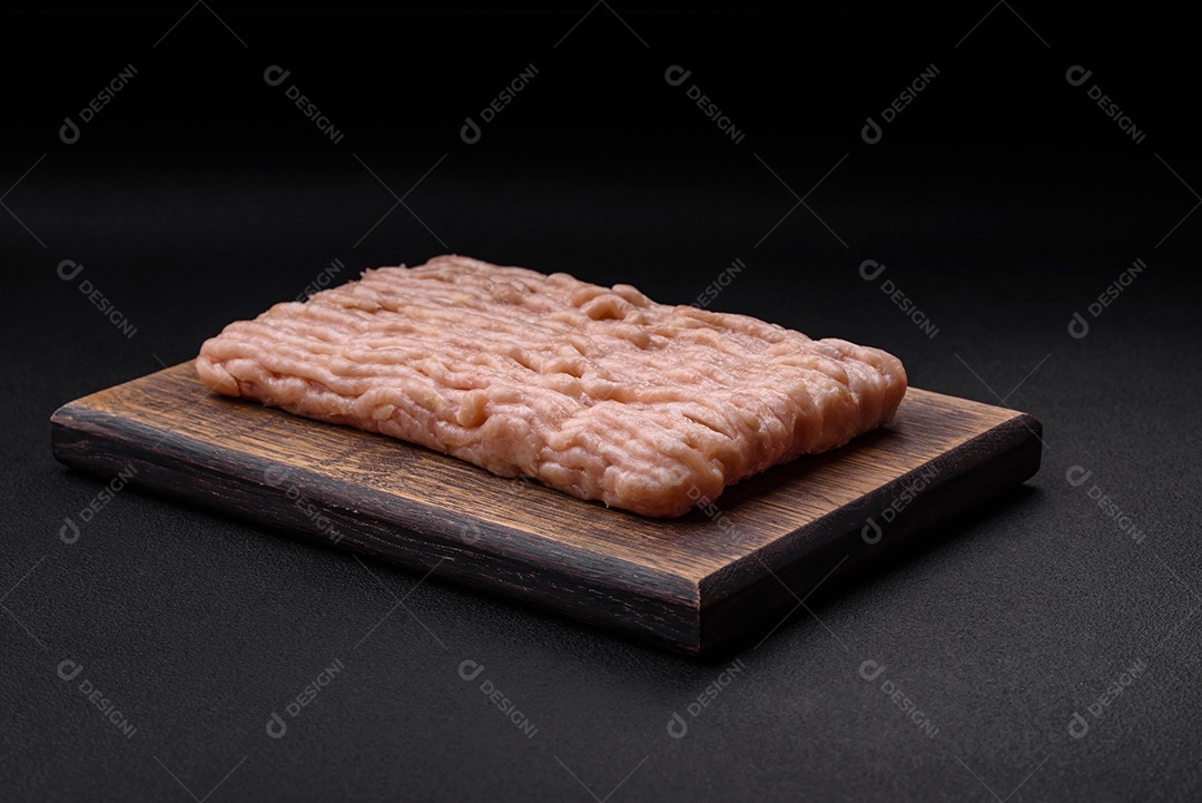 Frango picado fresco com sal, especiarias e ervas em uma tábua de madeira sobre um fundo escuro de concreto