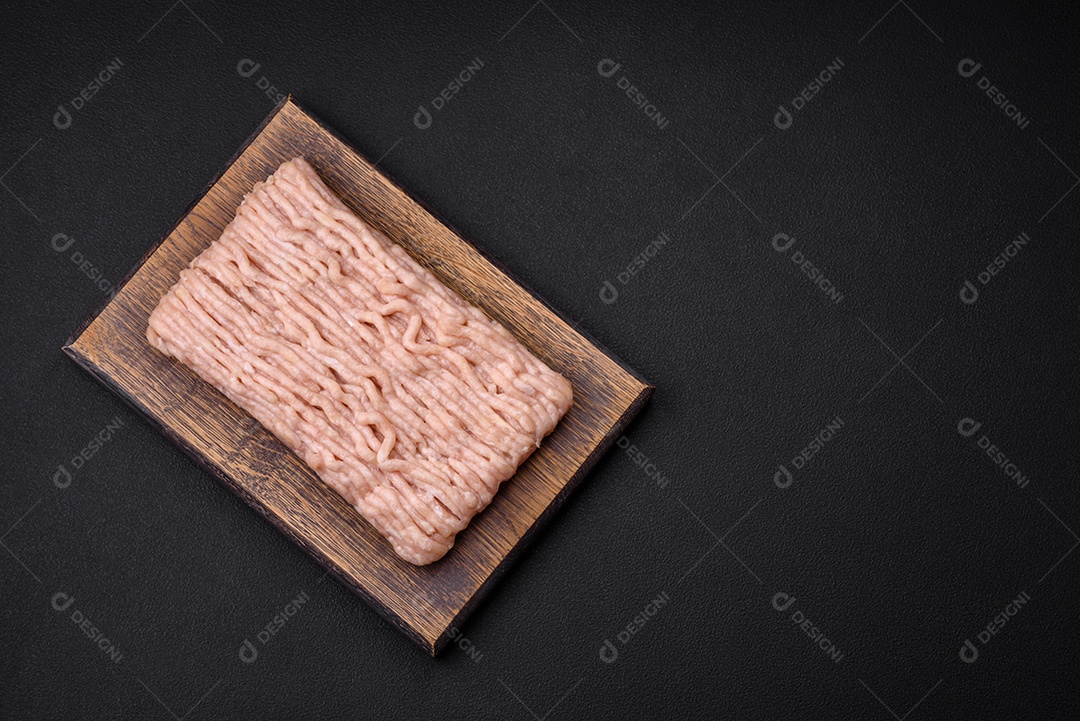 Frango picado fresco com sal, especiarias e ervas em uma tábua de madeira sobre um fundo escuro de concreto